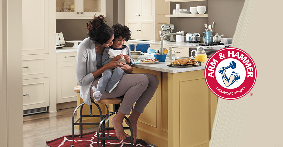 Child happily sits in his mother’s lap, as she sits on a stool at a kitchen counter with breakfast served. Arm & Hammer logo.