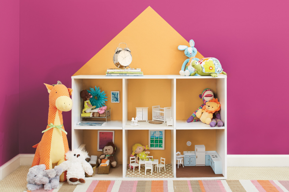 A dollhouse with stuffed animals and other toys sit in front of a magenta wall.