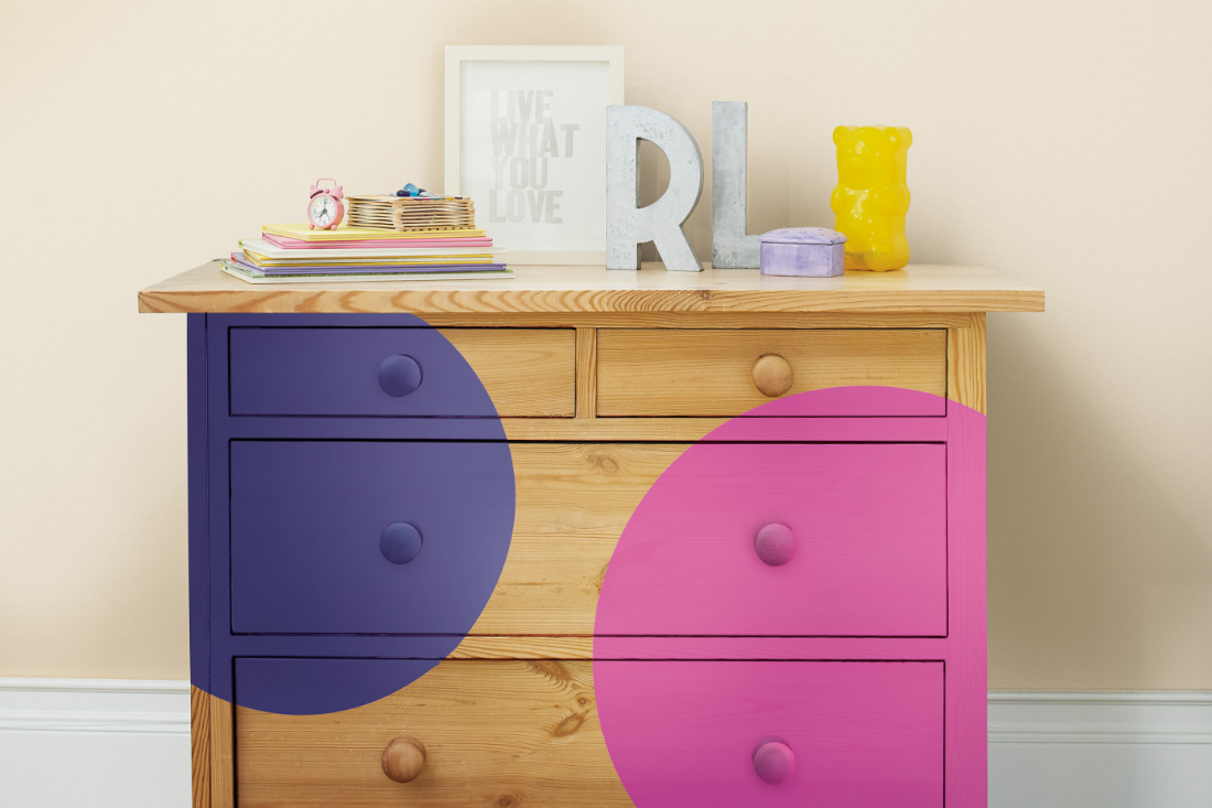 A warm wood bedroom dresser is painted with two large dots of color – one is purple and one is pink.