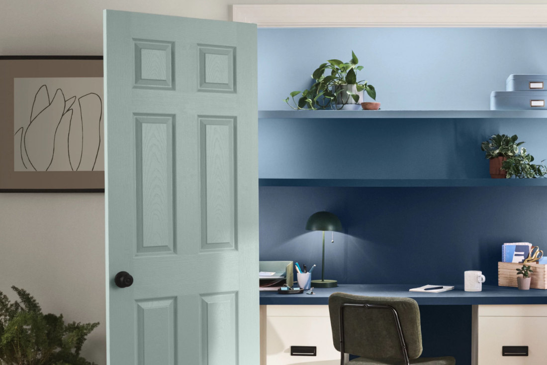 A home office inside of a closet with French doors painted light teal color. Wall and shelves in office are darker blue.
