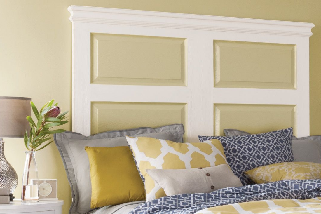 King size bed with patterned pillows and blankets sits in front of a wall painted with a yellow and white paneled headboard.