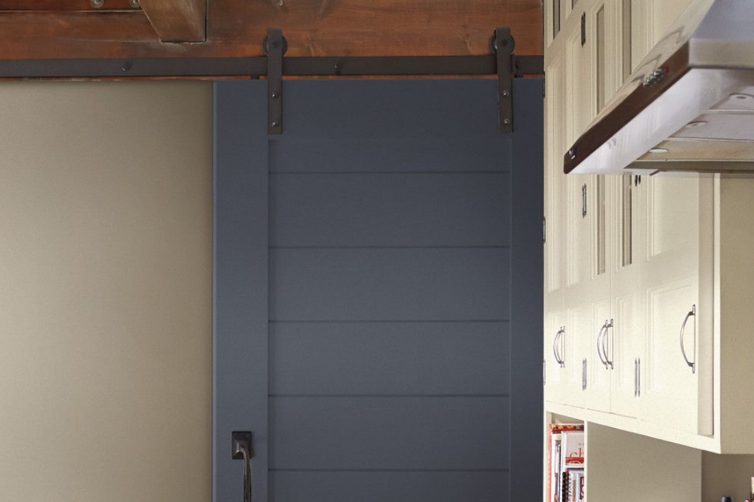 A barn door painted in the color flint stone, slides into a modern kitchen with light cabinets.