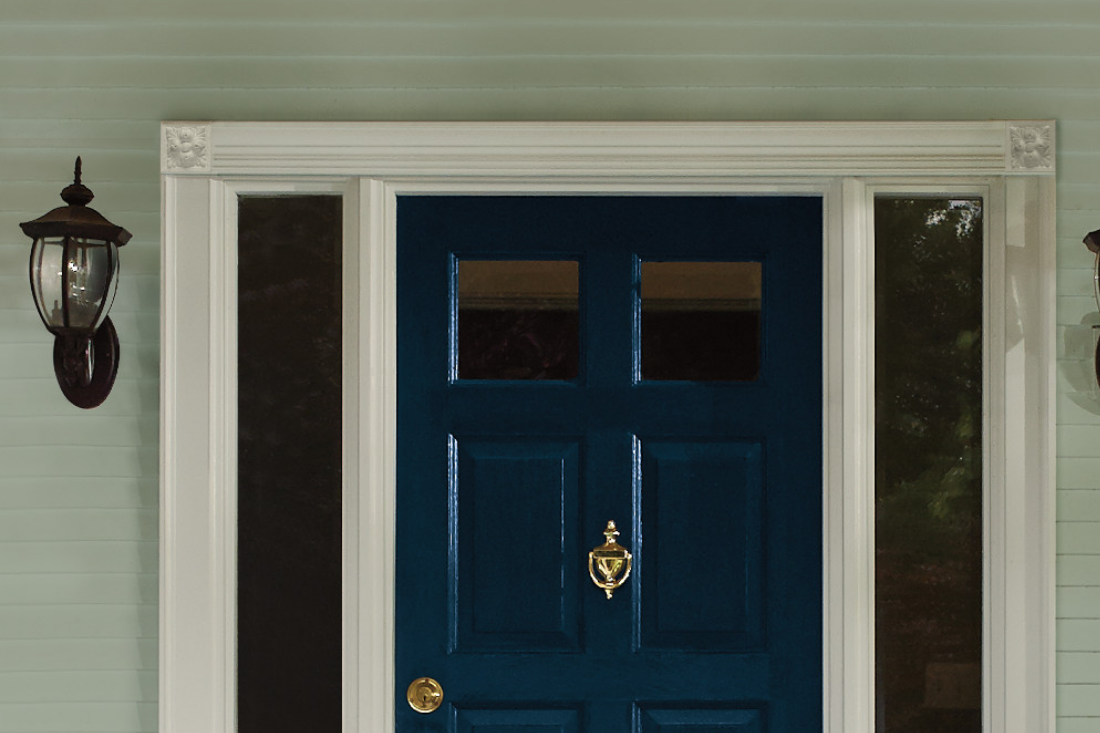 Front porch of a home with a blue front door and traditional gold handle and knocker, with teal siding.