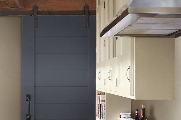 A straight-on angle of a barn door painted in the color flint stone, slides into a modern kitchen with light cabinets.
