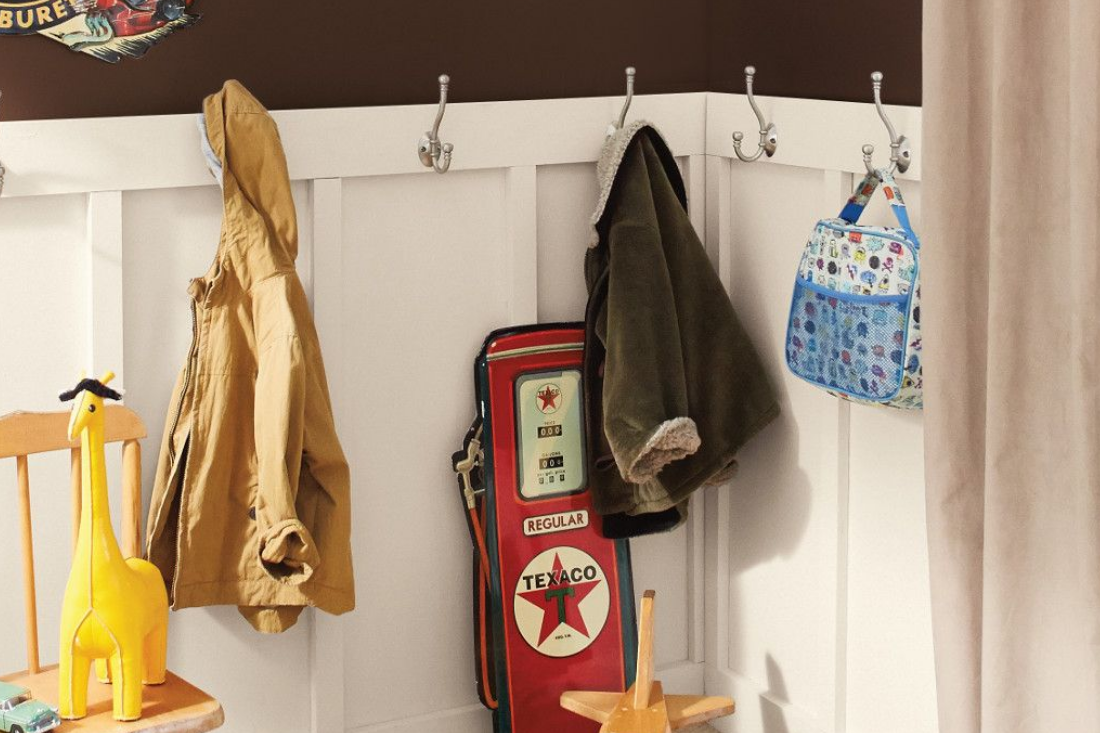 Mudroom with coats hanging on hooks and retro gas station signage with a brown colored wall and white wainscotting. 