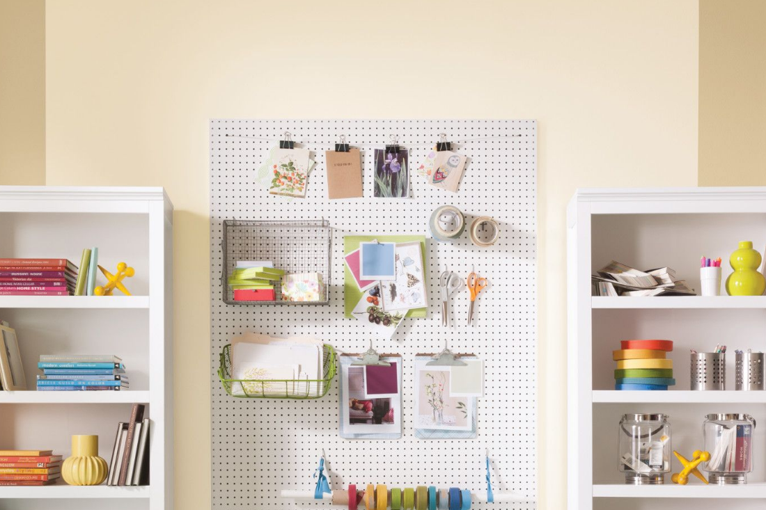 A smaller crafting room with shelving and pegboard holding multiple tools and accessories. Walls feature two hues of beige.