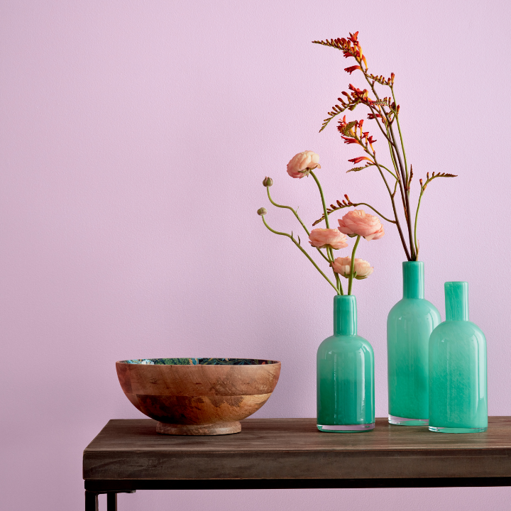 A wood console table with teal vases containing flowers and a wooden bowl sits against a wall painted sleepy purple.
