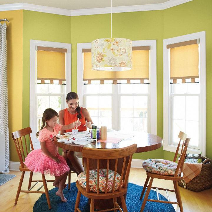 A mom and daughter crafting at a dining room table, large windows and a retro pendant light with praying mantis green walls.