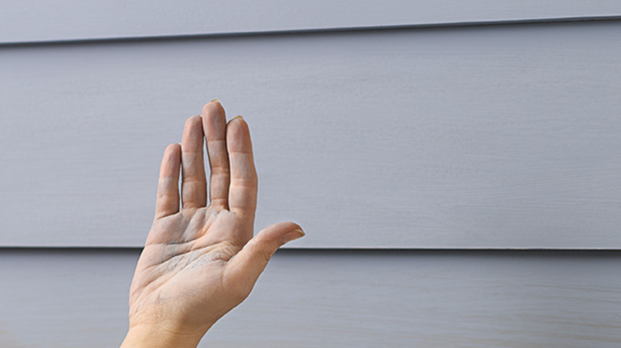 A hand covered in chalk and powder has just wiped the exterior siding of a home, showcasing its chalking condition.