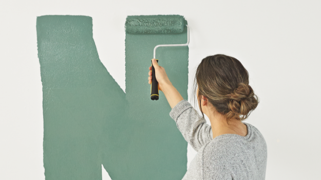  A woman applies green paint to a white wall with a paint roller.    