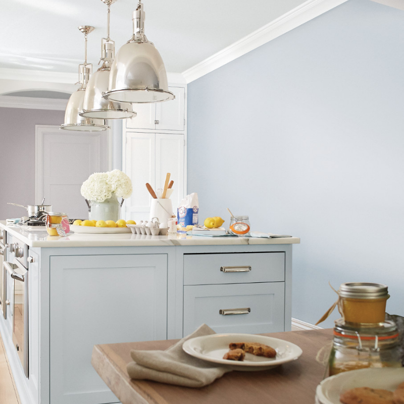 Large kitchen island with huge mirrored pendant lights above set for breakfast, cabinets and walls painted light blue.