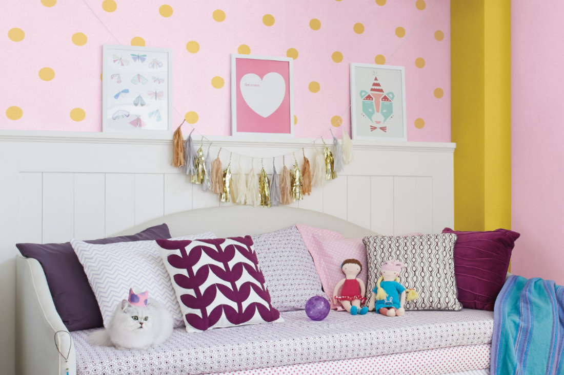 A nursery with trundle bed and pillows, a playful yellow polka dot pattern on a pink wall.