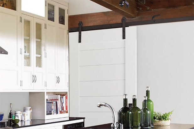 A barn door painted white slides into a modern kitchen with light cabinets.