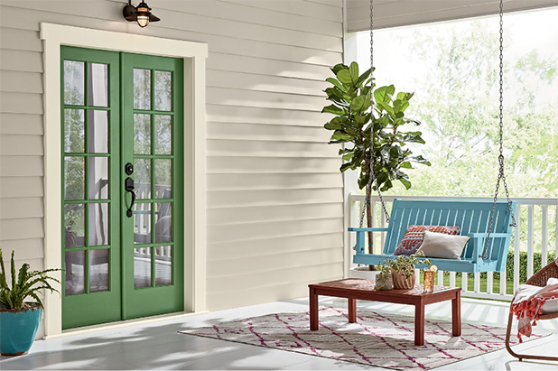 Sun-drenched, warmed silver deck with outdoor rug, coffee table and potted plants, with green-colored French doors.