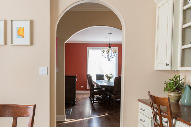 Two arched doorways lead from a kitchen into a dining room, painted the color French mustard.