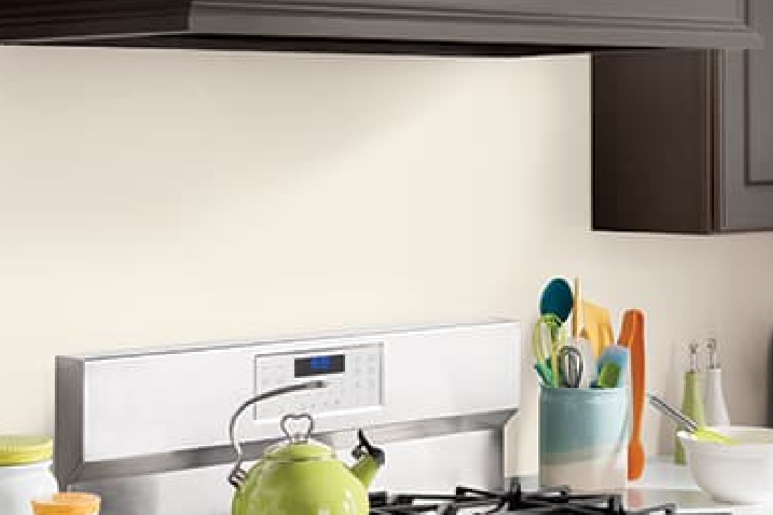 A kitchen stove top and range in white with a green tea kettle. Backsplash is painted in a light-colored semi-gloss paint.