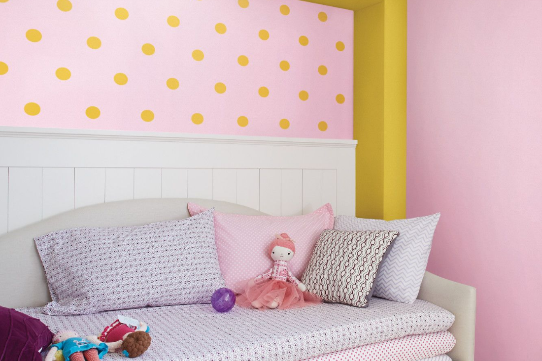 A nursery with a playful yellow polka dot pattern on a pink wall.